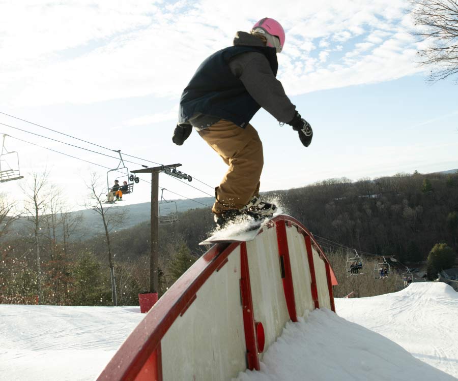 Snowboarder on rainbow rail in Stinger terrain park.
